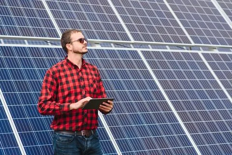 Young engineer with tablet computer standing near solar panels outdoors Foto stock