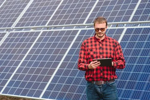 Young engineer with tablet computer standing near solar panels outdoors Stock Photos