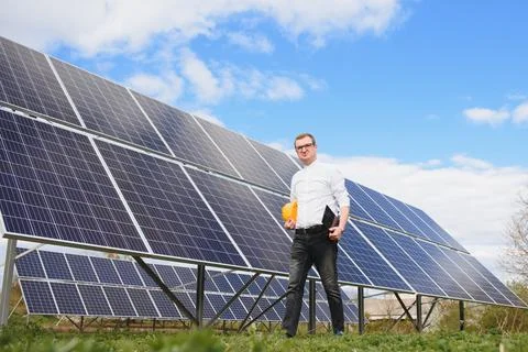 Young engineer with tablet computer standing near solar panels outdoors Foto stock