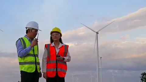 Young engineer team using walkie-talkie to checking system against wind turbine  Stock Footage 157857155