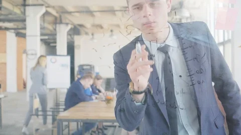 A young engineer writes formulas and graphs on a glass board using a marker Stock Footage 108977712