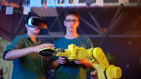 Young engineers with VR virtual reality headset controlling an yellow robotic Stock Footage 247485656