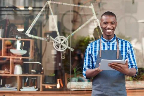 Young entrepreneur using a tablet in front of his cafe Stock Photos