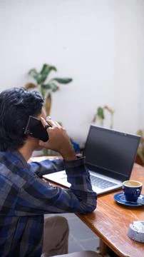 Young Entrepreneur Working on Laptop While Talking on Smartphone in Cafe Stock Photos
