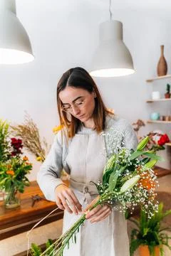 Young ethnic female employer composing gentle flowers bouquet in florist stor Stock Photos