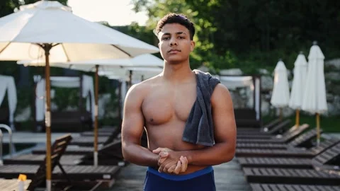 Young ethnic man standing poolside in swimwear with towel, ready for summer swim Stock Footage 328160046