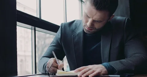 A young European man taking notes in the café by the window Video stock 74790145