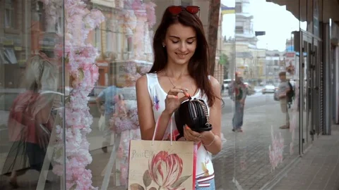 Young exciting brunette stands near a shop in the street and pulls out her phone Stock Footage