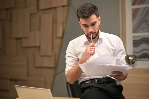 Young executive looking at documents puzzled while sitting at his desk Stock Photos