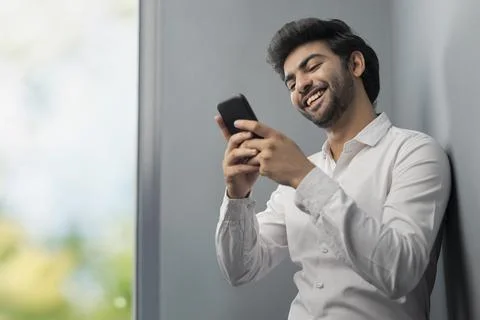 A YOUNG EXECUTIVE SMILING AND USING MOBILE PHONE DURING BREAK TIME	 Stock Photos