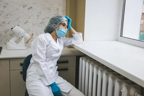 A young exhausted dentist sits by the window, reflecting on a long day of work. 写真素材