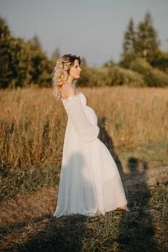 A young expectant mother in the third trimester of pregnancy in a white dress Stock Photos