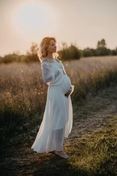 A young expectant mother in the third trimester of pregnancy in a white dress Stock Photos