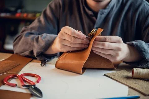 A young experienced shoemaker or tailor sews a unique piece of leather in a Stock Photos