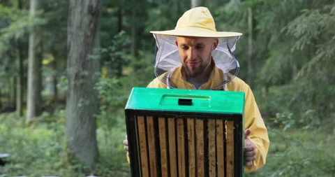A young experienced smiling man engaged in beekeeping holds an apiary of bees in Stock Footage 165029016