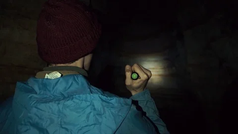 Young explorer walking in cave with hand flashlight. Deep darkness around Stock-Footage 80063493