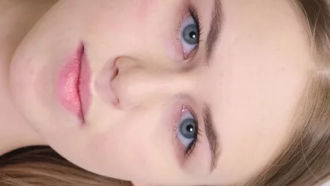 A young fair-haired girl is looking at the camera while standing on a light Stock Footage 250356322