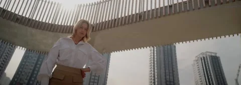 Young fair-haired woman posing against backdrop of high buildings, 4k slowmo Stock Footage 220194876