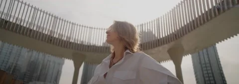 Young fair-haired woman posing against backdrop of high buildings, 4k slowmo Stock Footage 220195374