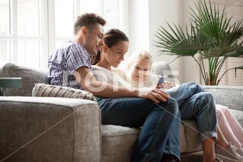 Young family with daughter using mobile app sitting on couch Stock Photos