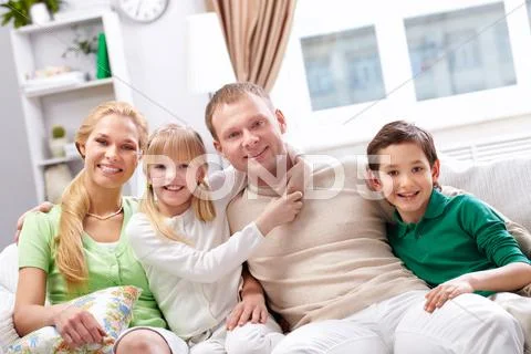 A young family of four sitting on sofa, looking at camera and smiling Stock-Fotos