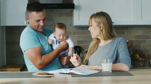 Young family in the kitchen. Mom reading a book, with the baby daddy is near Stock Footage