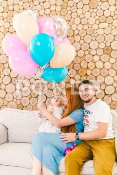 Young family man, woman and baby girl sitting on couch indoors with wooden de Stock Photos