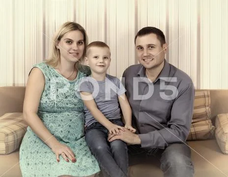 Young family is resting at home on the couch. A pregnant mother, a small son Stock Photos