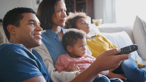 Young family sitting together on the sofa in their living room watching TV, Stock Footage