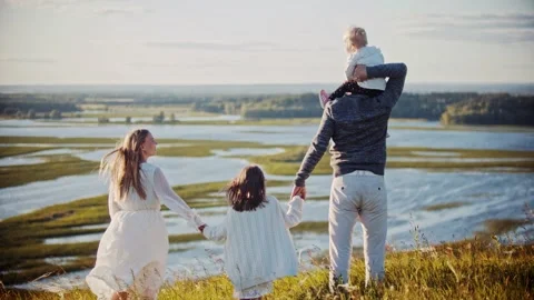 Young family standing on the field and holding hands while looking at river Stock Footage 135968341
