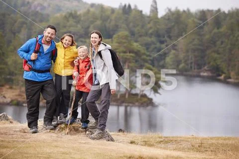 Young family standing on a rock by a lake looking to camera embracing, full l Stock Photos