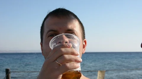 Young fat man drinking beer and eatsfast food near the sea Видео 97098455