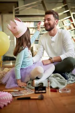 A young father enjoys putting on make-up with his daughter while they prepare Stock Photos