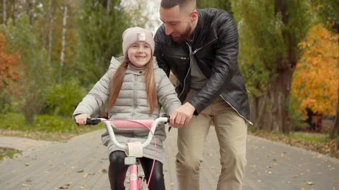 Young father having fun with his daughter riding a bike in the autumn park Vidéo 147396768