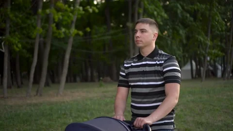 A young father is pushing a stroller through the park. A man walks in nature Stock Footage 208026231