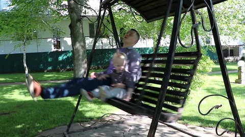 The young father is riding on a swing with his son. Concept of a happy family an Stock Footage 89877083