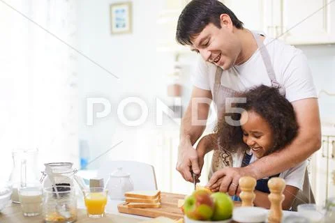 Young father showing his daughter how to cut bread Stock Photos
