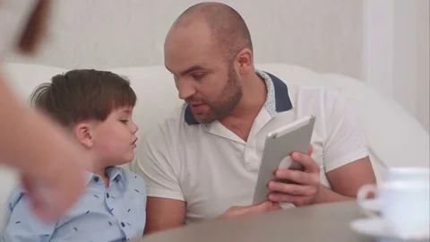 Young father showing something on the tablet to his wife and sons 스톡 동영상 76582718