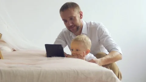 A young father shows something on a tablet to his little son Stock Footage 82919756
