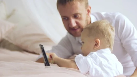 The young father shows something on the tablet to his little son. Dad hugs his Video stock 82926592
