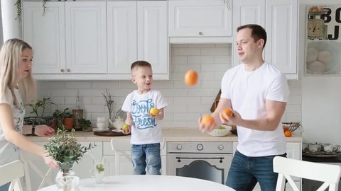 A young father shows the son in the kitchen how to juggle oranges Stock Footage