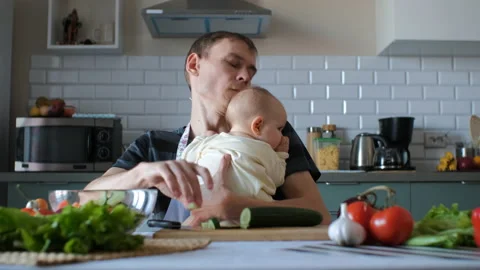 Young father slicing cucumber while holding baby Stock Footage 227921655