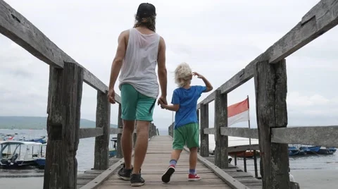 Young father with son walking along wood bridge holding by hands on the sea pier Stock Footage 68030232