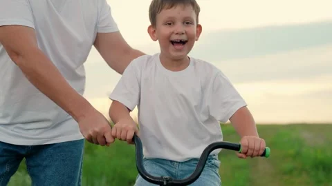 Young father teaches child to keep balance while sitting on bicycle. Childhood Stock Footage 252157087