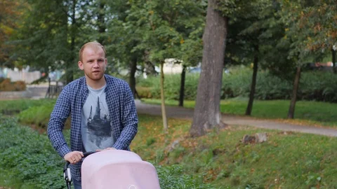 Young father walks roll a stroller with baby child on a city park alley green Stock Footage 118533730