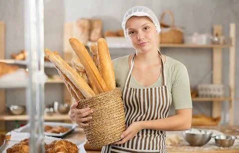 Young female apprentice baker holding basket of baguettes Stock Photos