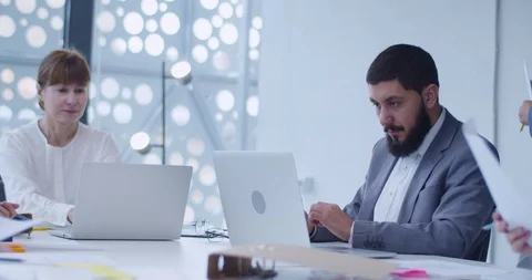 Young female assistant handing documents to man and woman at laptop computers Stock Footage 129517470