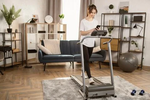 Young female on automatic treadmill for exercise talking in a video chat on a 스톡 사진