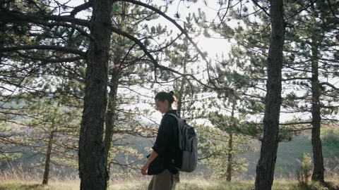 A young female with a backpack walks through the autumn forest during sunset. Stock Footage 283464467