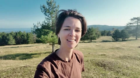 Young female blogger talking to camera outdoors in a mountain meadow. Natural Stock Footage 325742505
